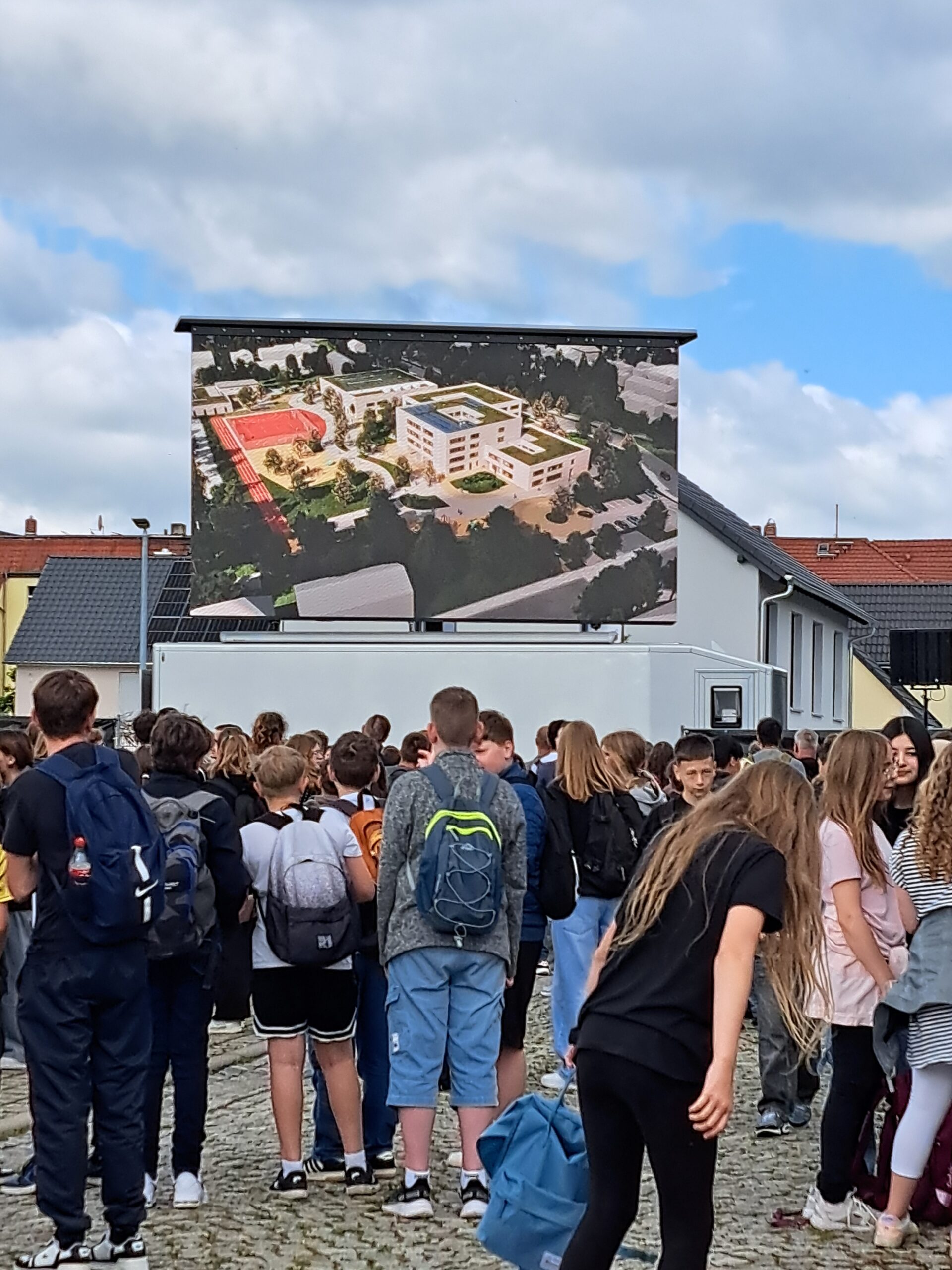 Schülerinnen und Schüler auf einem großen Platz vor einer Leinwand mit Visualisierung des künftigen Bildungscampus Naumburg